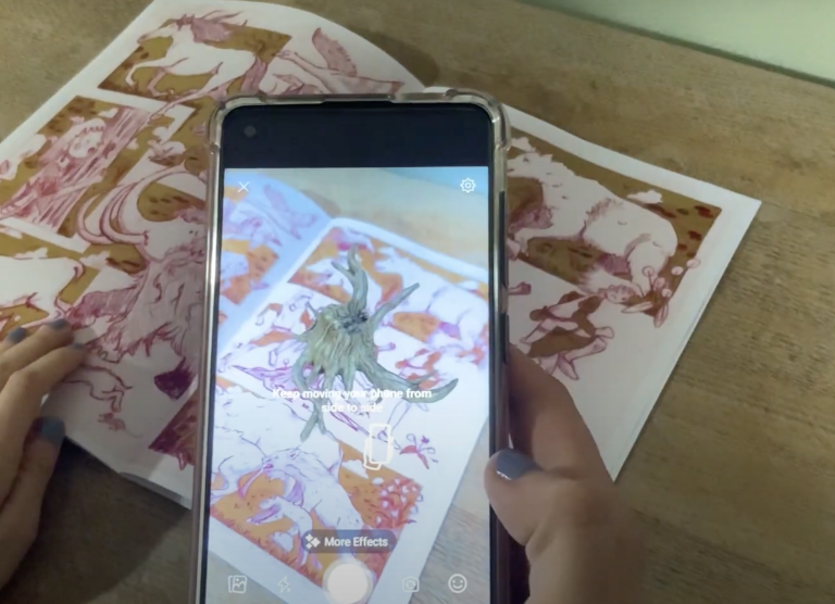 Close up of Indianna Williams' work; an augmented reality feature is demonstrated on a phone, with an illustration in the background.