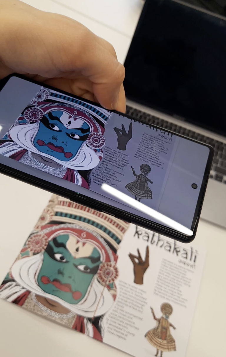 Close up of Indianna Williams' work; an augmented reality feature is demonstrated on a phone, with an illustration in the background.