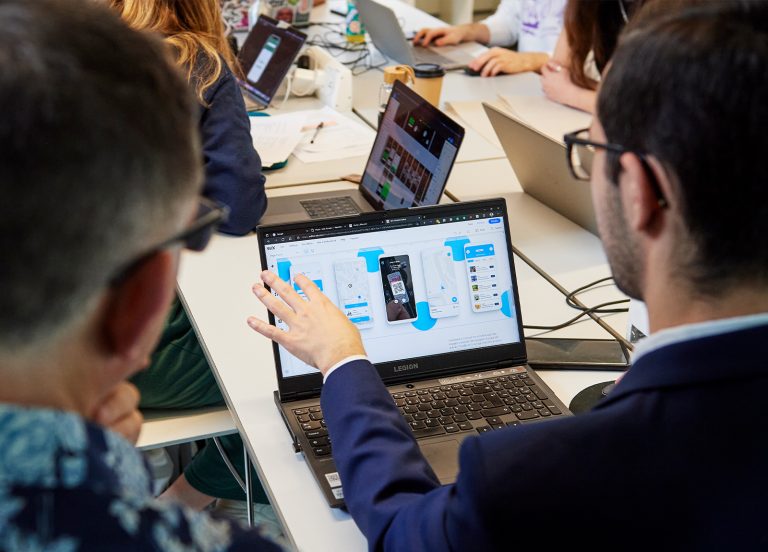 Two people discussing work on a laptop at a table with people working