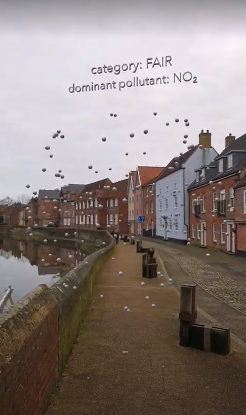 A photograph of a riverside footpath lined by multicoloured houses. A series of dots can be seen superimposed over the image, from an augmented reality system.