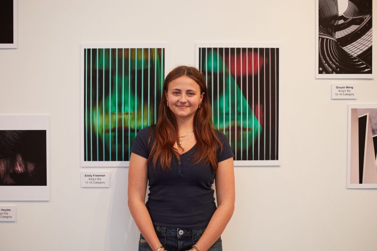 Photograph of a person in a black t shirt. She stands in front of two photographs.