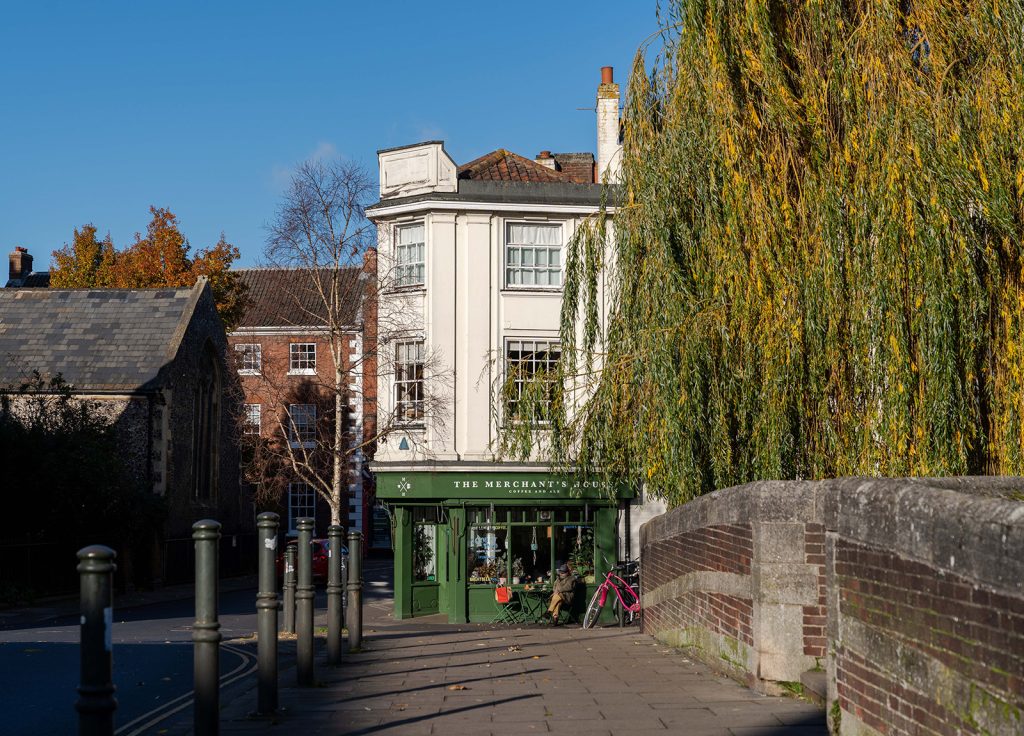 Photograph of Merchants House exterior. A cafe with a dark green facade on the corner of a street. A stone wall and bollards lead up to the cafe.