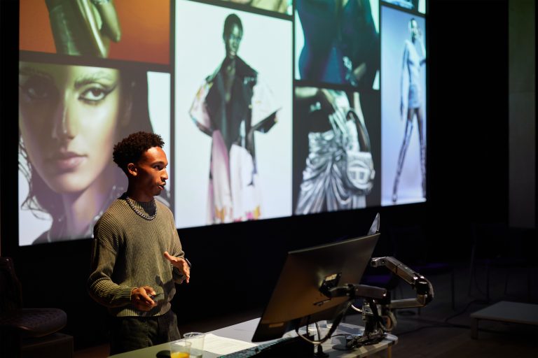 A person is presenting from the front of a lecture theatre; a collage of images is on the screen behind them.