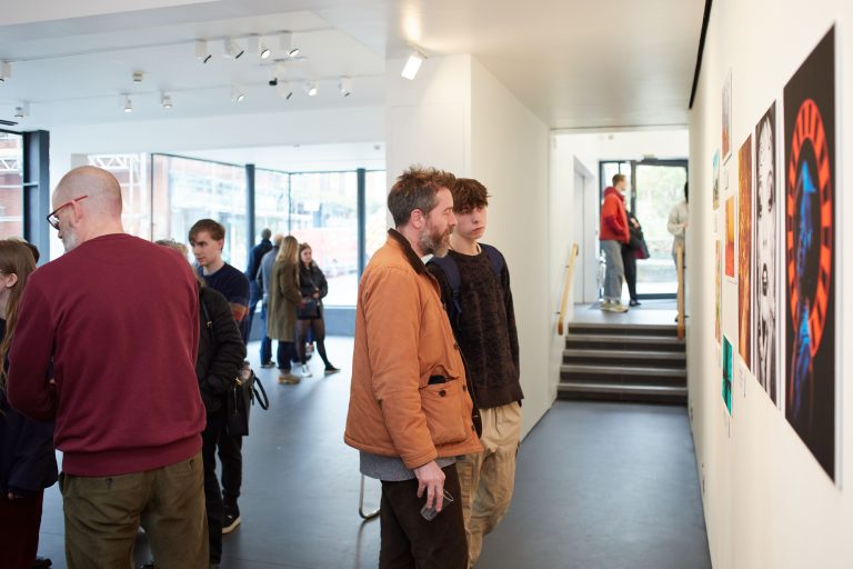 Two people are standing next to each other looking at a gallery wall. They can be seen in profile with the wall to the right.