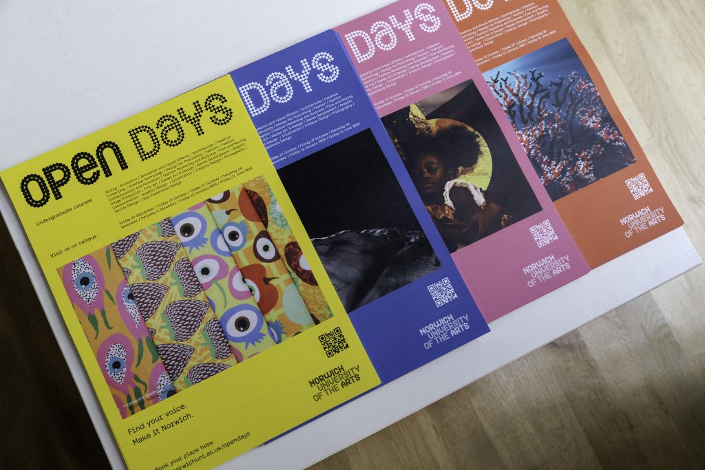 Open Day posters on a white table. The four posts are yellow, blue, pink and red with various images and information written on them.