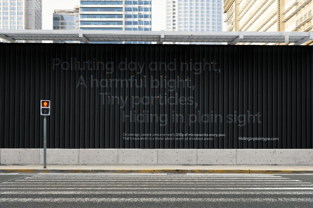 A large billboard with the text: "Polluting day and night. A harmful blight. Tiny particles, Hiding in plain sight." Below it reads: "On average, people consume nearly 260g of micro-particles every year. That’s as equal to a dinner plate's worth of shredded plastic.