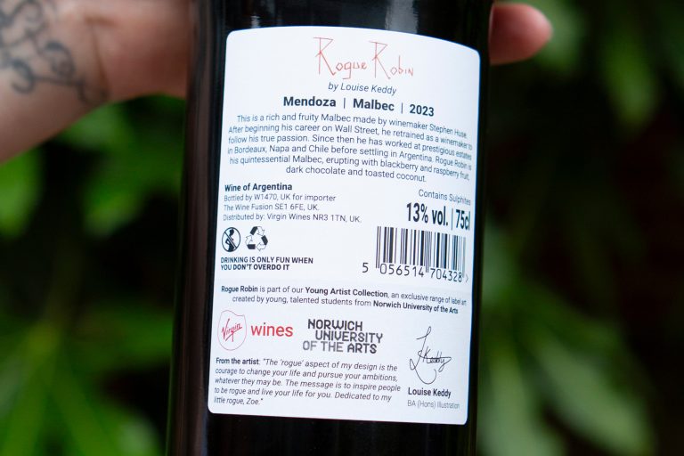 A close-up of the back label of a wine bottle. The label includes details about "Rogue Robin, Mendoza Malbec 2023," the artist Louise Keedy and logos for Norwich University of the Arts.