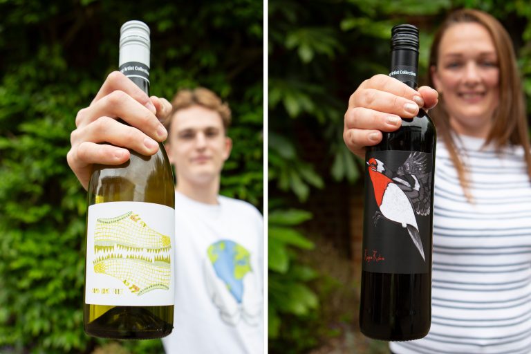 Two individuals hold wine bottles towards the camera. The left bottle is white wine with a yellow label, and the right bottle is red wine with a bird illustration on the label. Both are set against a backdrop of green foliage.