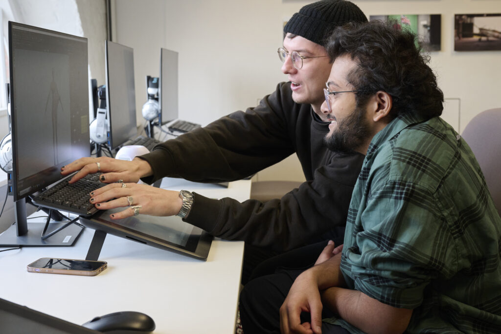 Two people sat at a computer helping one another