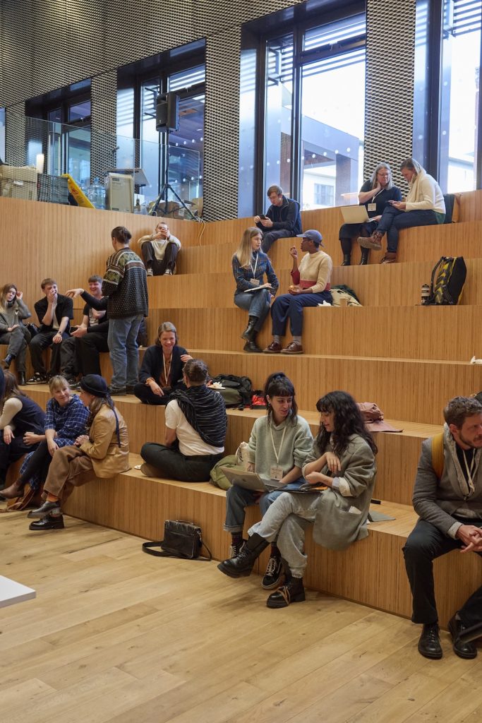 A group of conference attendees gather on wooden steps, drinking coffee and conversing.