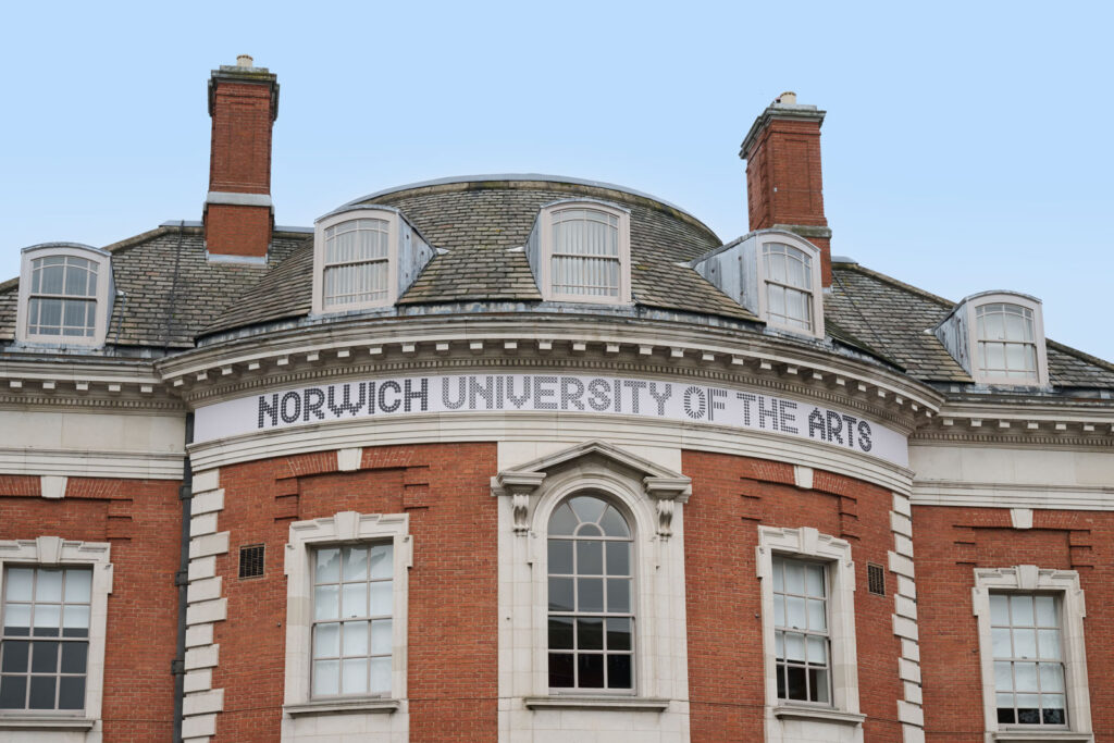 A photo of Bank Plain, one of Norwich University of the Arts' campus buildings. The photograph shows an aluminium Norwich University of the Arts logo upon a plinth, around the top of the building