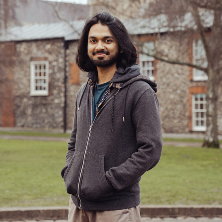 Norwich University of the Arts international student, Shrey Bansal, from India, stands in the Norwich Cathedral grounds, with the cathedral behind him.