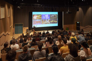 Visiting speaker Mark Brown is presenting in front of a big screen at the front of a busy lecture room.