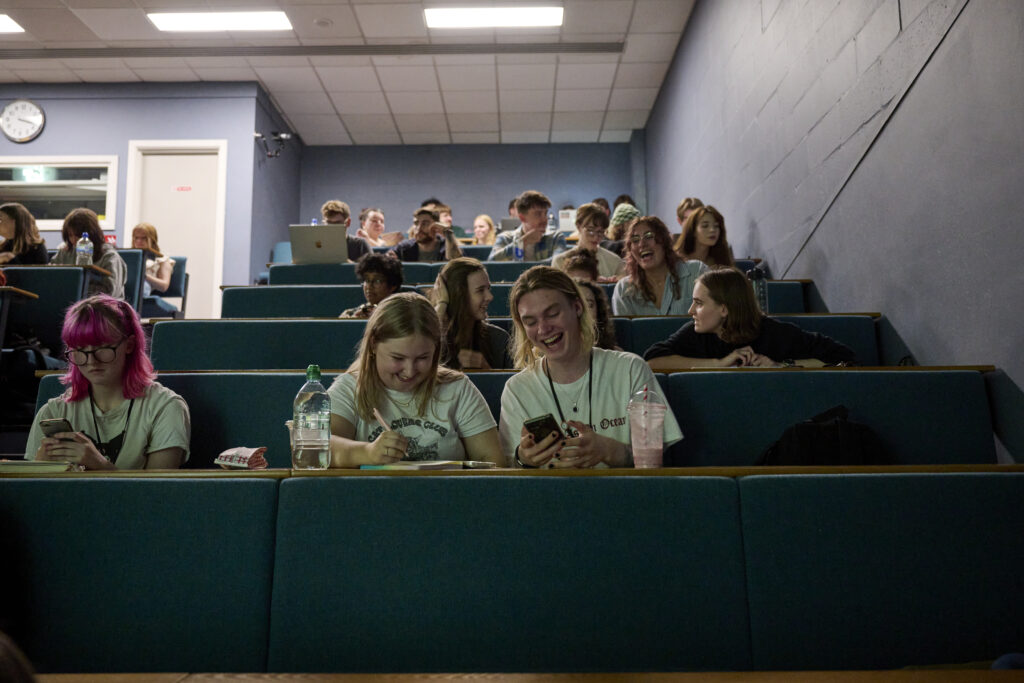 A group of students in a lecture theatre laughing, chatting and smiling