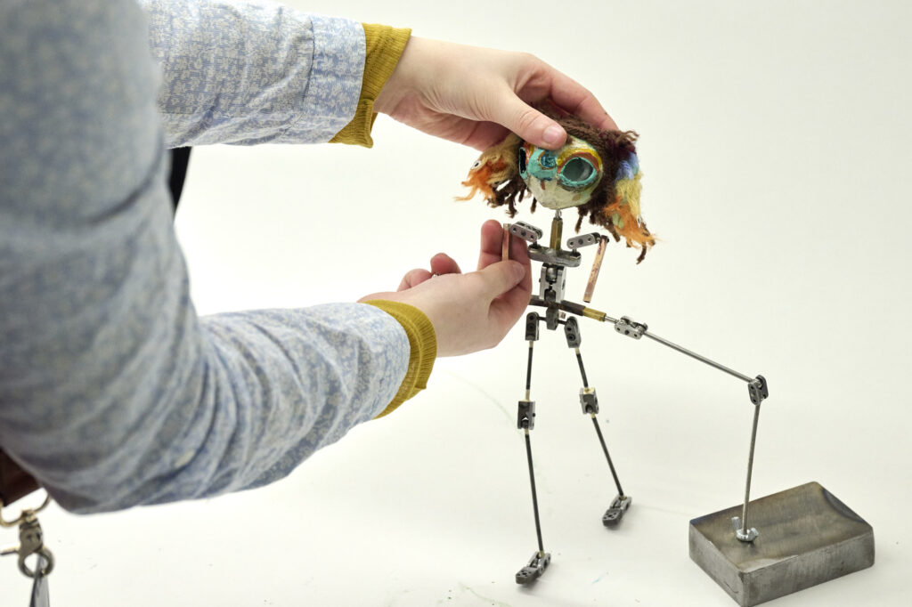 A photograph of a student's hands adjusting a puppet attached to a base.