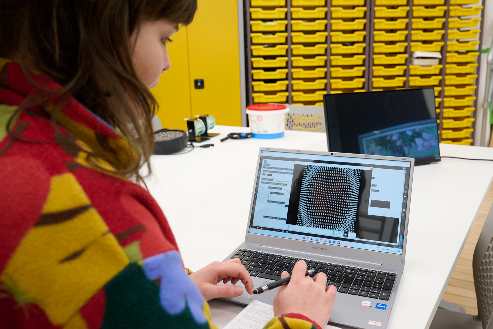 A student photographed from over the shoulder, working on their laptop creating motion design from coding