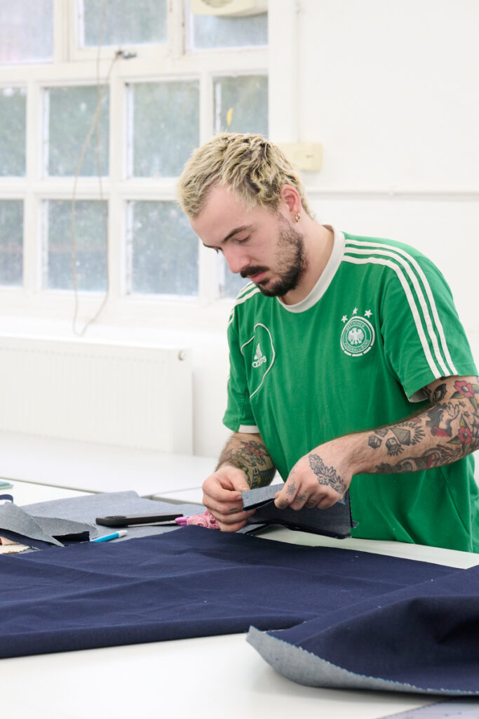 A photograph of a student in the fashion workshop piecing together patterns of cut fabric upon a table