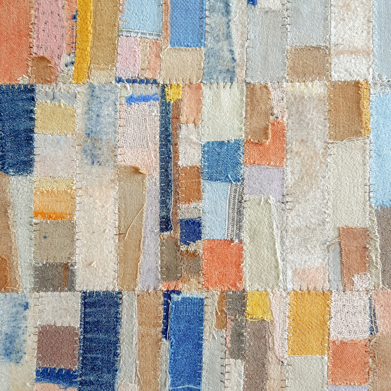 A close up photograph of a tapestry made of several scraps of coloured fabrics, with visible stitching to create a patchwork effect.