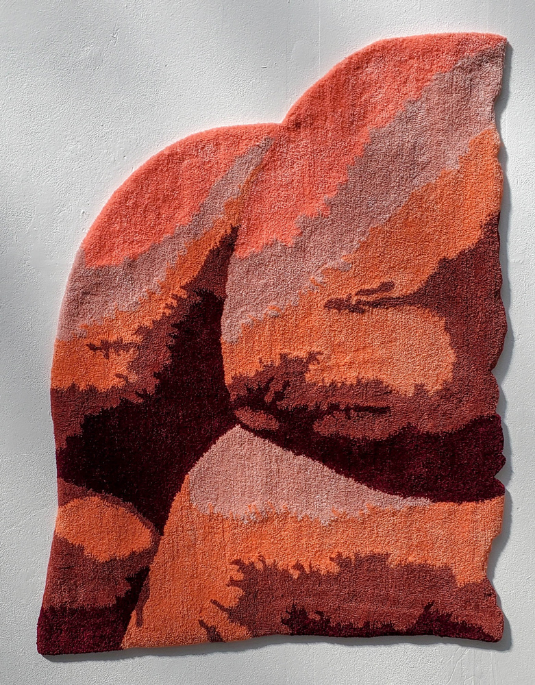 A photograph of a rug cut into the shape of glutes. The rug depicts a landscape scene made from orange, mauve, purple and grey fabric