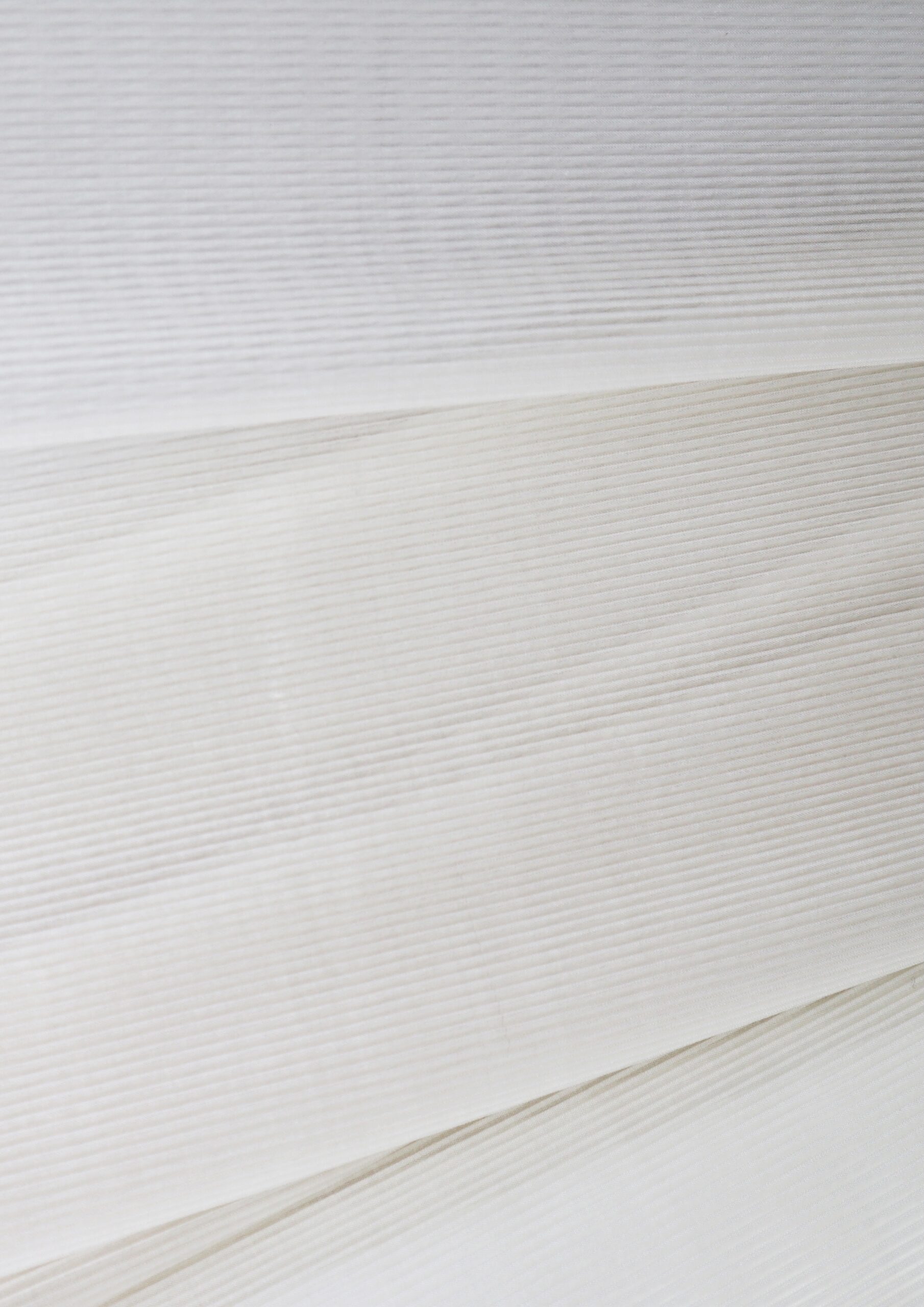 Close-up of several layers of thin, white and off-white fabric or paper with fine horizontal lines and subtle texture, creating a soft, minimal, and slightly striped appearance.