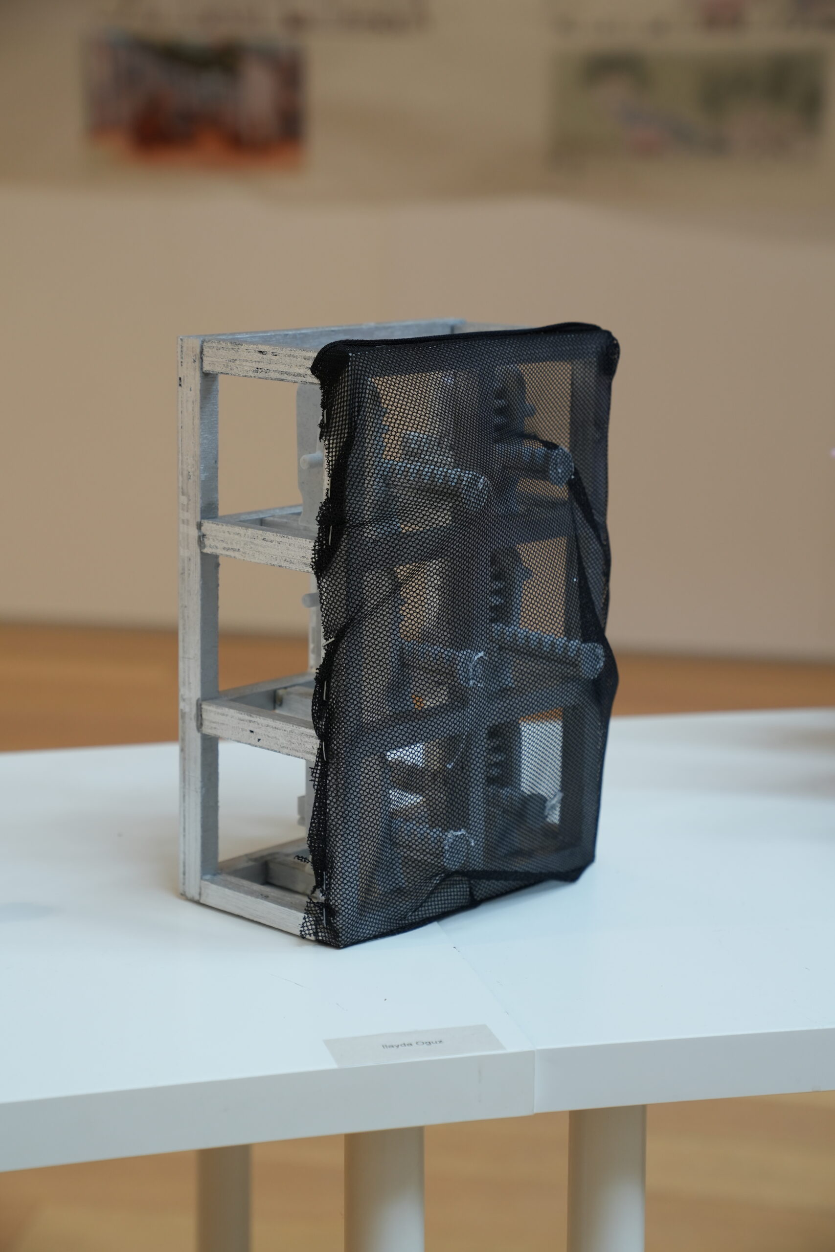 A rectangular metal sculpture covered partially with black mesh sits on a white display table.