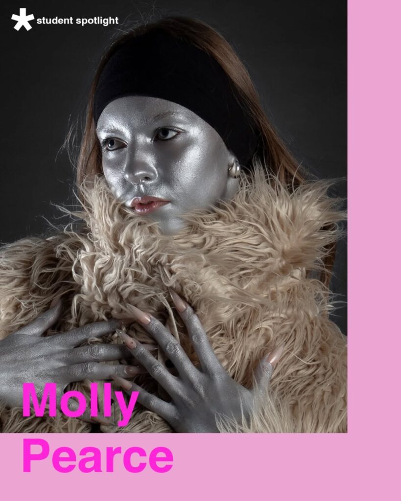 A person with silver-painted skin and lips, wearing a fluffy beige coat and black headband, poses against a dark background. Text reads “student spotlight” and “Molly Pearce” in bright pink on a pale pink border.