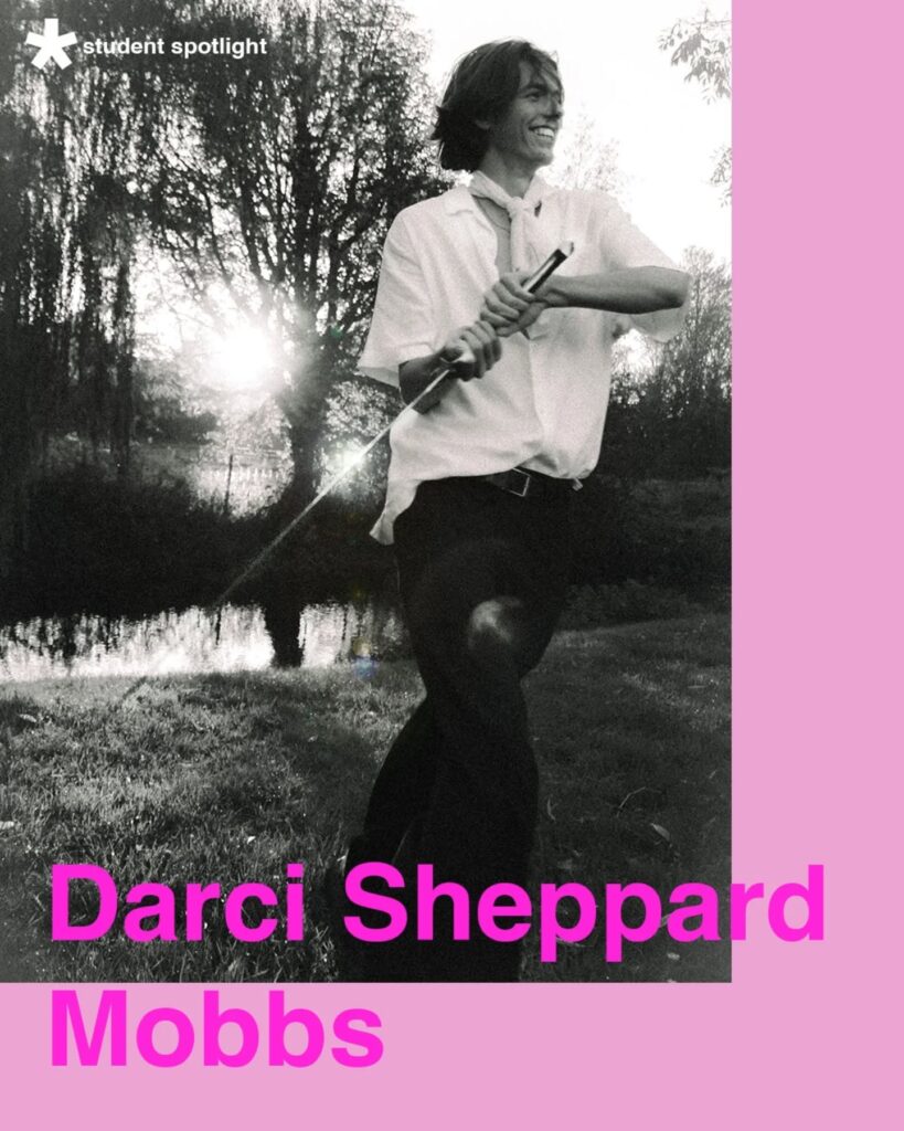 A black-and-white photo of a young person smiling while playing drumsticks outdoors near a pond, with sunlight streaming through trees. Text reads: "student spotlight Darci Sheppard Mobbs" on a pink background.
