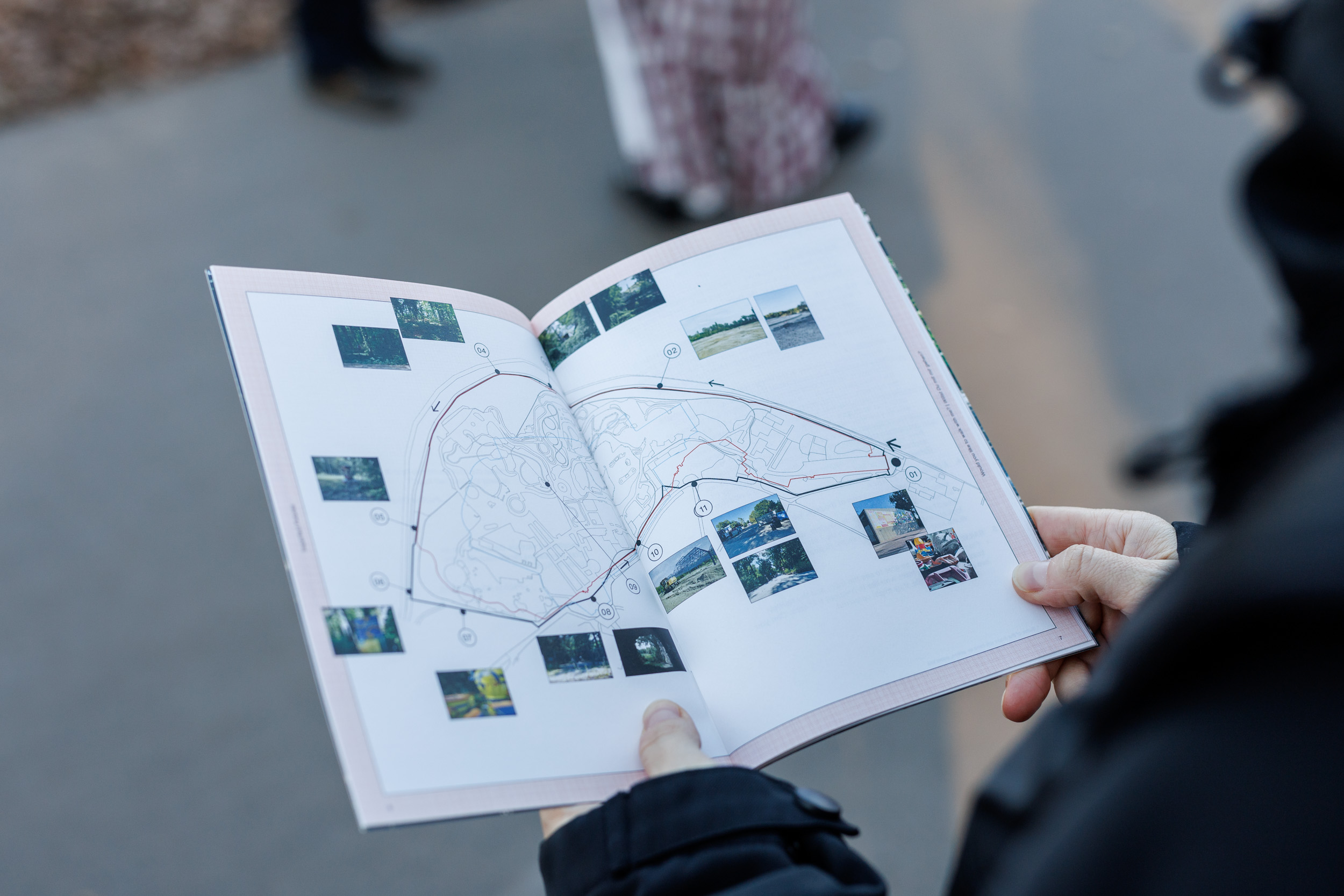 A person holds an open booklet displaying a map with a marked route and small photos along the path. The background is blurred, focusing on the map and images within the booklet.
