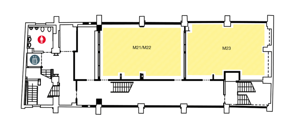 Floor plan showing two large yellow rooms labeled M21/M22 and M23. Stairs are at both ends. Toilets and an elevator icon are at the left, near the entrance; the restrooms are marked with male and female symbols.