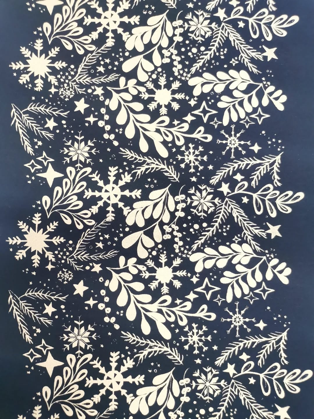 White snowflakes, stars, and leafy branches create a festive, intricate pattern on a dark blue background, evoking a winter or holiday theme.