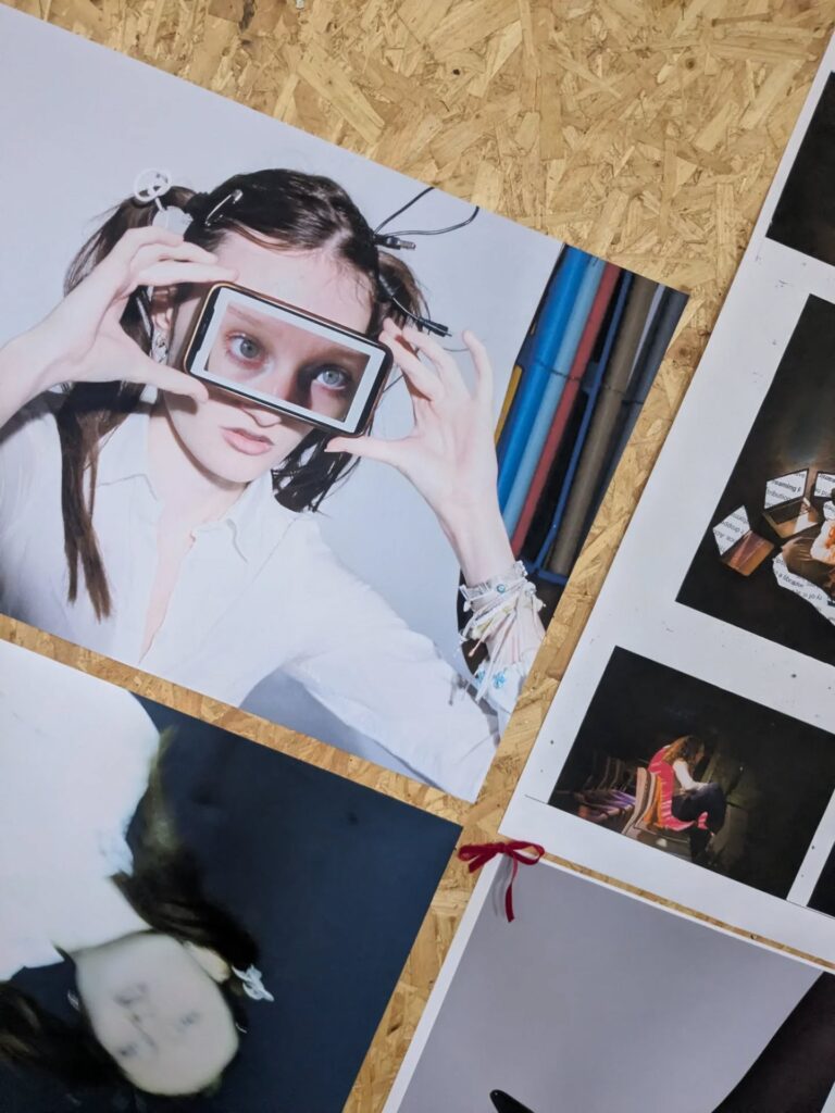 A display board with various photos, including a woman holding a rectangular frame to her face, partially magnifying her eye, and other colorful artistic images arranged closely together.