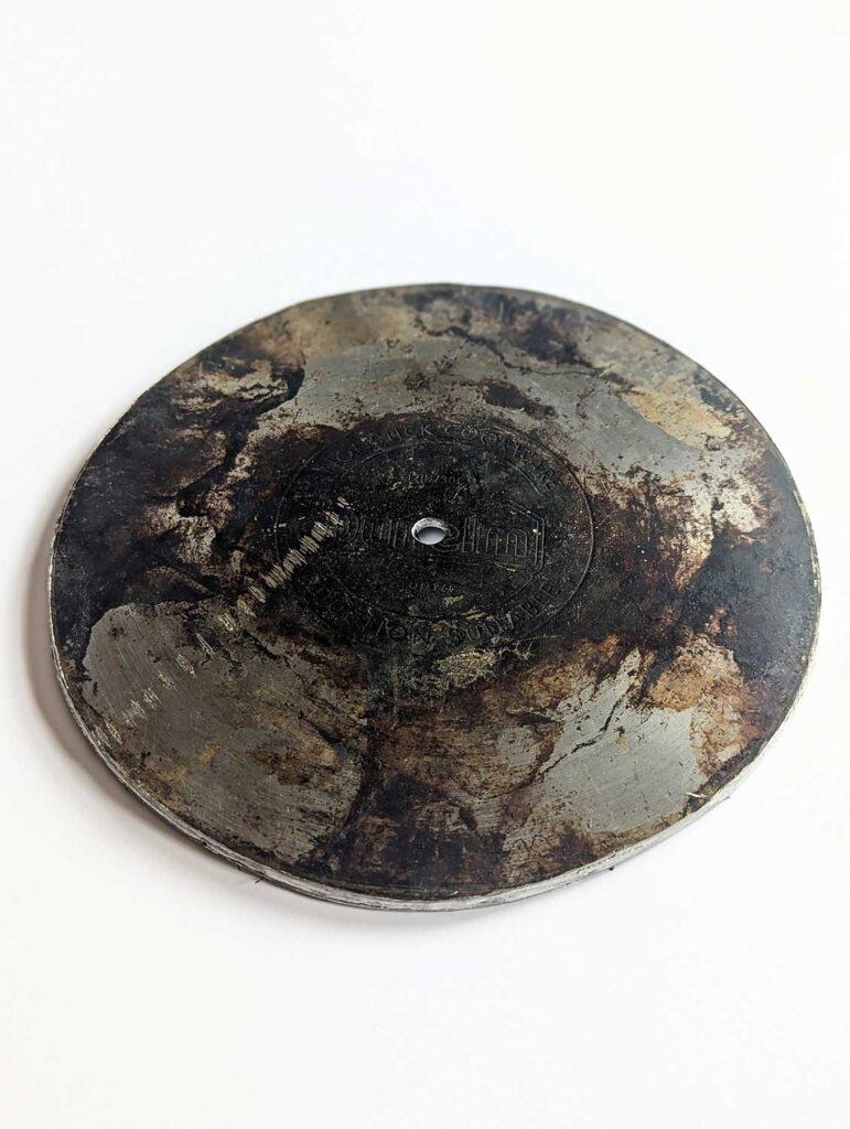 A metal disc with a hole in the center, lying flat on a white surface. Faded markings are barely visible on its surface.