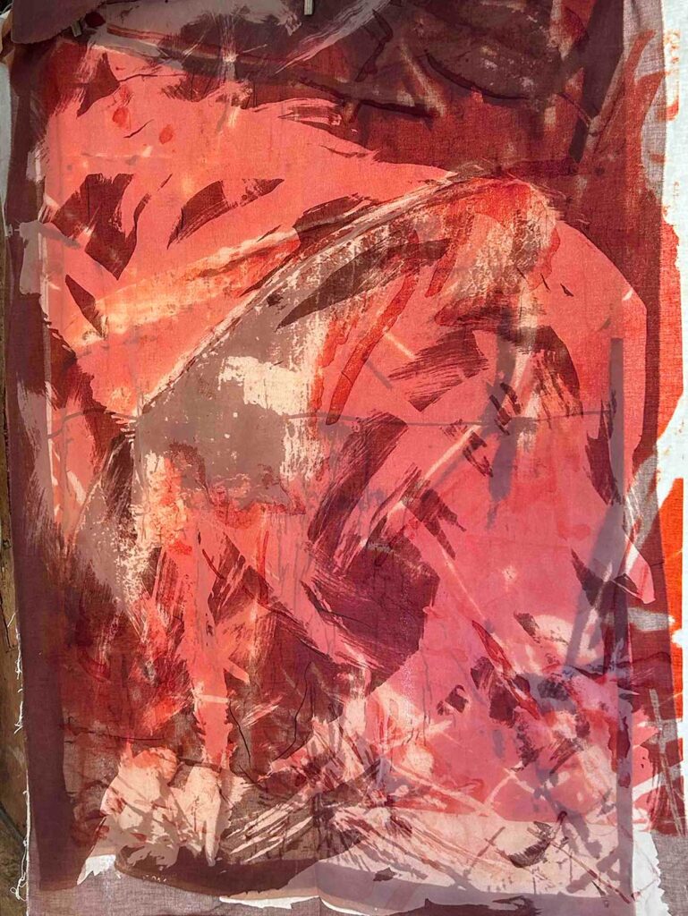 Abstract colours on fabric, featuring bold, sweeping brushstrokes in shades of red, pink, and brown.