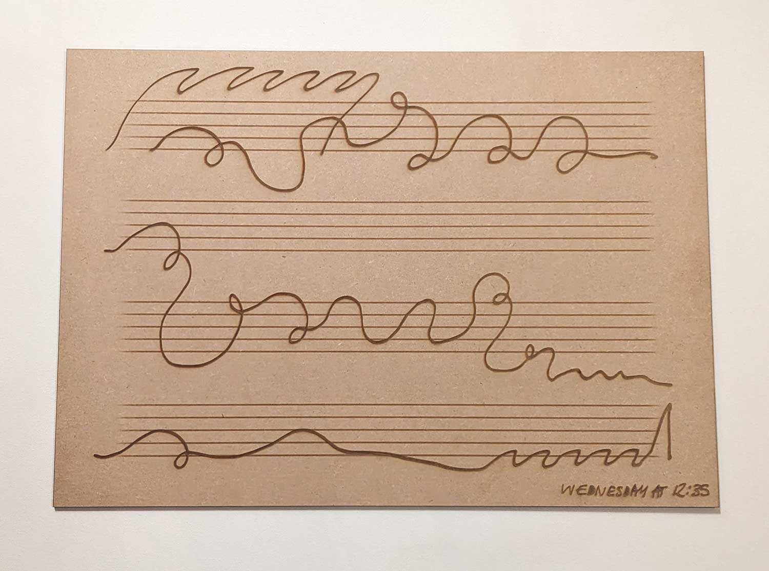 A piece of brown paper with four sets of parallel horizontal lines, resembling a musical staff, and wavy, irregular lines drawn across each staff in brown ink. The bottom right corner has text which reads: Wednesday at 12:35.