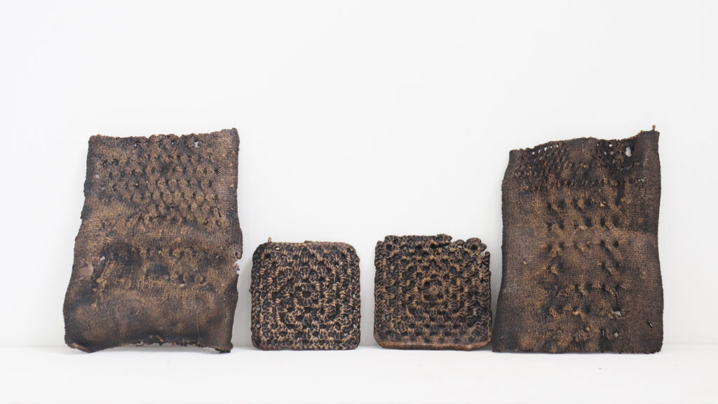 Four rectangular and square pieces of dark, textured, and slightly charred material stand upright against a white background. Their perforated, honeycomb-like patterns create a striking visual—perfect inspiration for our upcoming Online Open Day.