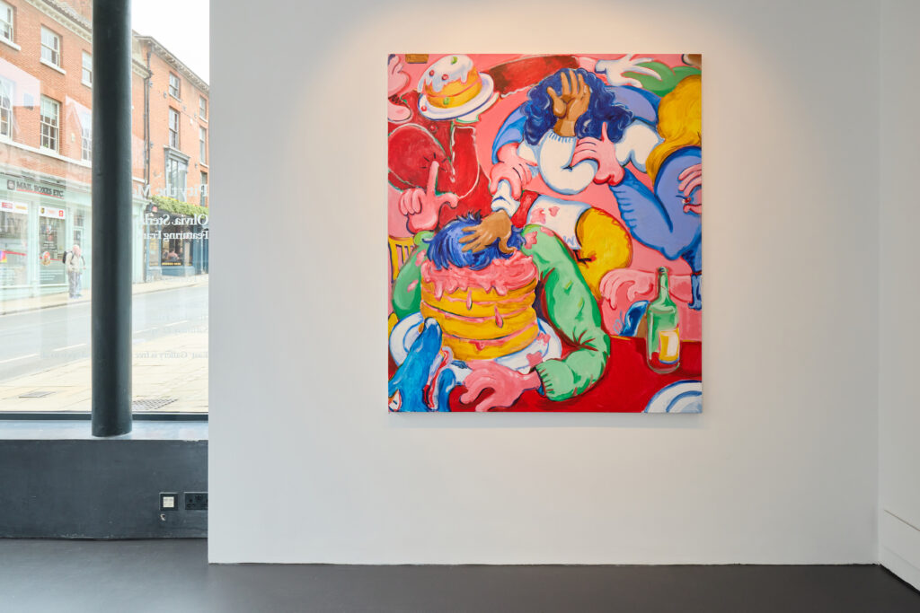 A colorful painting hangs on a white gallery wall, depicting abstract figures with exaggerated hands pushing faces into a pink cake, surrounded by chaotic party elements and bold colors like red, blue, and yellow.