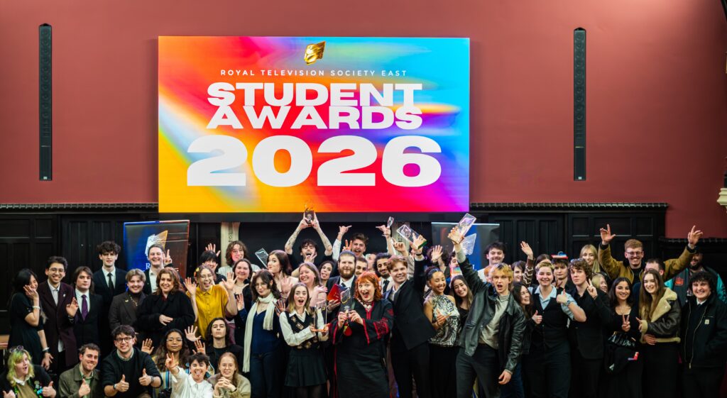 A large group of people celebrate in front of a colorful screen that reads "Royal Television Society East Student Awards 2026." Some hold trophies and certificates, and many are smiling, cheering, or giving thumbs up.