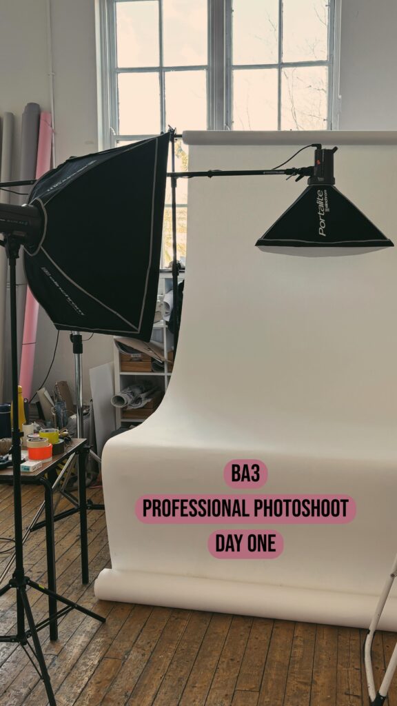 A photography studio setup with large softbox lights and a white paper backdrop. Text on the image reads: "BA3 Professional Photoshoot Day One.