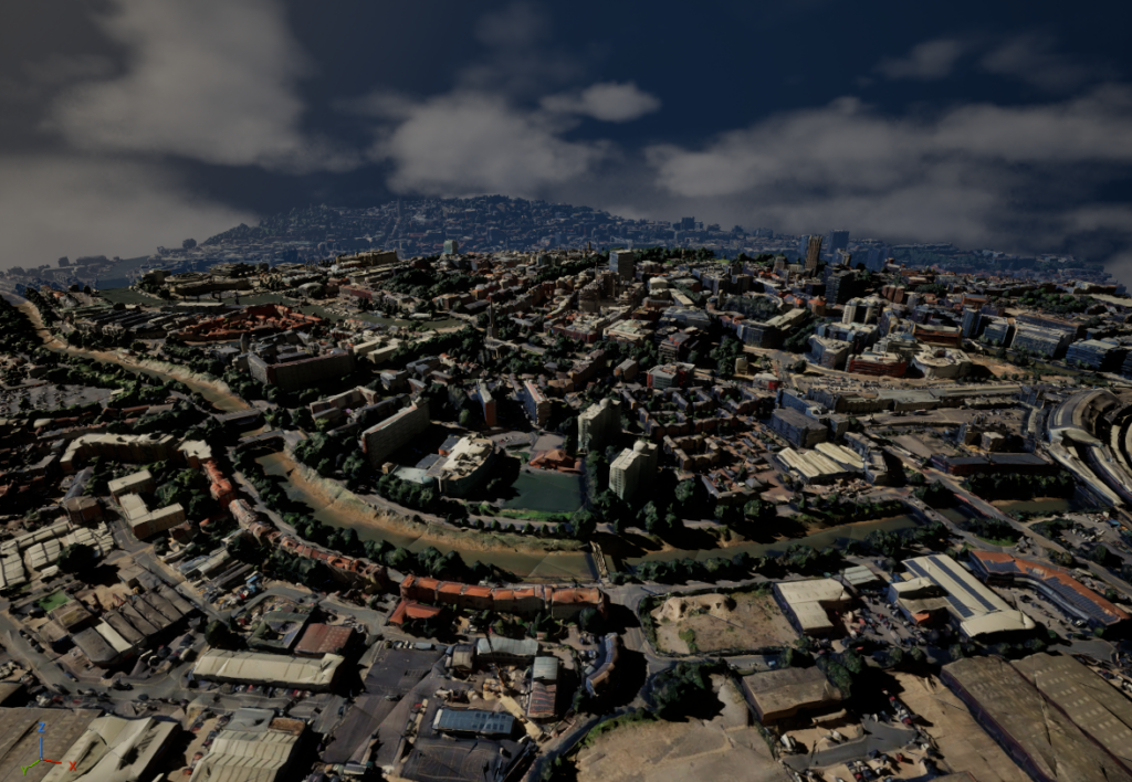 Aerial view of a city with dense buildings and green spaces, surrounded by hills under a partly cloudy sky, with mountains visible in the background.