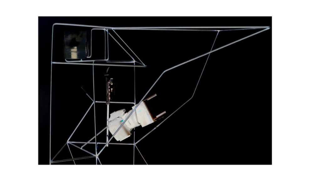 A geometric wireframe sculpture with intersecting lines and two white, angular objects attached, set against a black background with a white border.