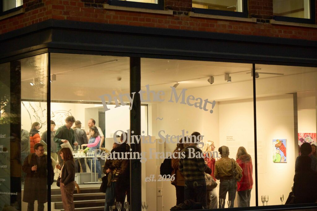 People gather inside and outside a brightly lit art gallery at night. The window displays text for an exhibition: "Pity the Meat! Olivia Sterling featuring Francis Bacon est. 2026." Artworks are visible inside.