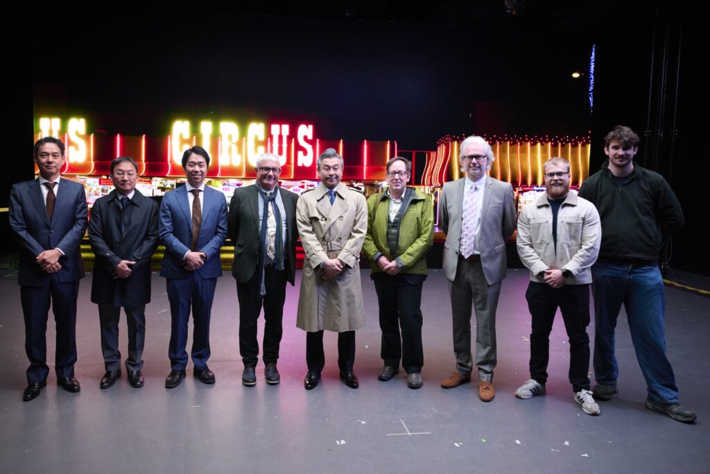 Nine people standing in a row in front of a brightly lit "CIRCUS" sign, dressed in a mix of business and casual attire, posing for a group photo on a stage or event floor.