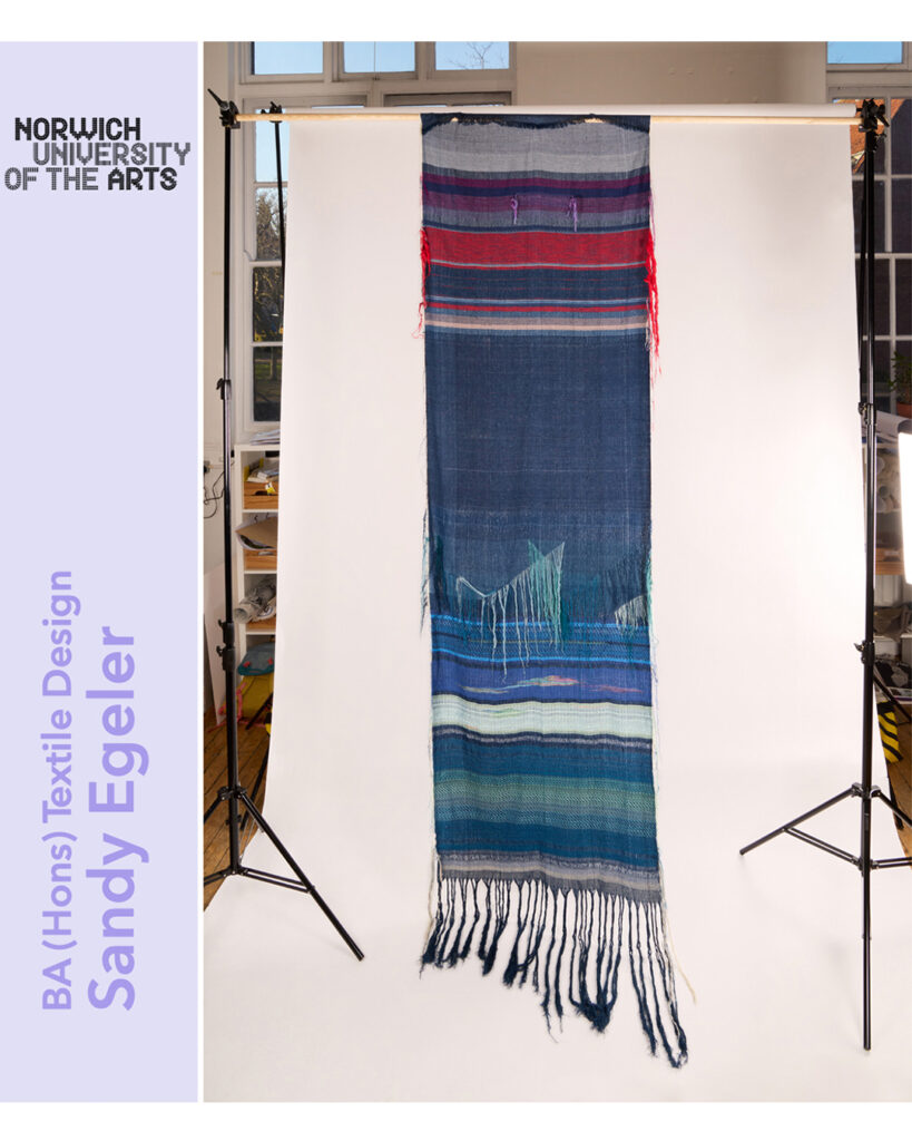 A long woven textile with blue, green, red, and white stripes and fringed ends hangs in a studio. Text reads: "Norwich University of the Arts, BA (Hons) Textile Design, Sandy Egeler.
