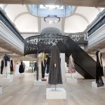 Photo of NUA building Boardman House atrium with a black metal circular staircase in the centre and many clothing mannequins around the lower level featuring a variety of BA Fashion clothing items