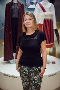 photo shows Brand and Editorial Manager at Jarrold, Emma Harrowing smiling at camera with blonde bob hair and black loose top with various fashion designs on mannequins in the background