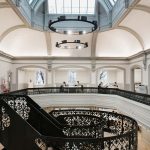 photo of NUA building boardman house shows large atrium with circular staircase in center with upper level wall with black metal railing and large white curved walls