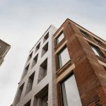 photo looking up at NUA building Cavendish House shows tall grey smooth tiled building with red brick addition and several windows against sky background