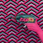 Image of a pink patterned background with a pink hand holding a laser gun with the words ZAP written on