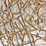 Image of lasercut wooden letters hanging on a wall, stitched together with tape