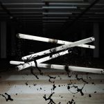 Image of four tubes of strip lighting hanging in the air with black paint being dropped on them from above